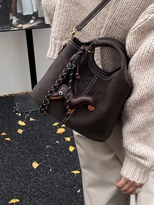 Retro dark brown suede bucket bag with white stitching and cute dog charm on autumn leaves