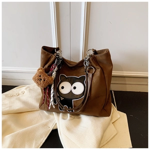 Détail d'un sac cabas marron avec broderie de chat et pendentif ours en peluche