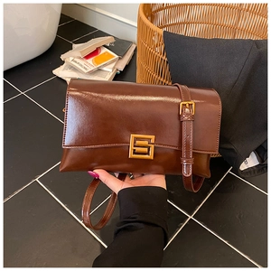 Detail of a brown glossy leather shoulder bag with a gold square buckle and strap