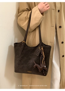 Detail of dark brown suede tote bag with dachshund charm and gold fashion lettering