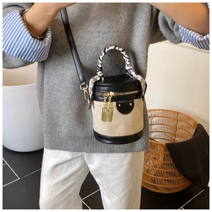 Model wearing a cylindrical bucket bag with beige quilted suede and black leather finish