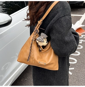 Detail of a brown leather tote bag with a woven rope charm and a plush leopard bow bear