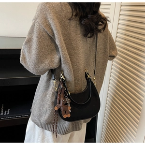 Détail du sac hobo noir avec breloque ours et sangle London sur un pull gris chic
