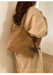 Detail of a brown suede tote bag with golden lettering and a cute dog charm accessory