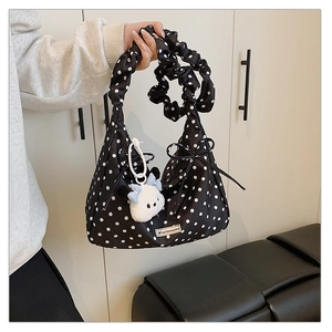 Detail of black polka dot handbag with pleated handle and cute white puppy plush charm
