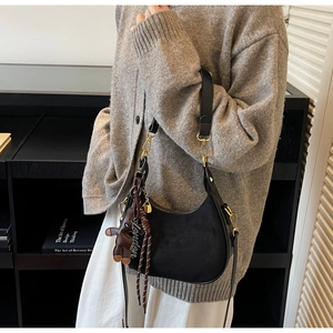 Détail du sac bandoulière noir en forme de croissant avec quincaillerie dorée et breloque