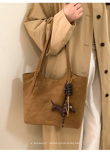 Close-up of brown suede tote bag with dachshund pendant and gold logo detail