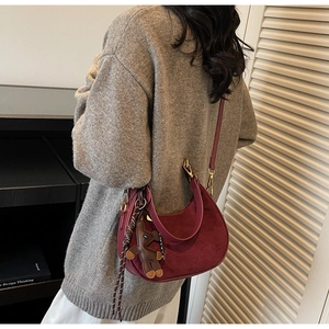 Vue détaillée du sac hobo bordeaux en daim avec breloque ours porté à l'épaule par un mannequin