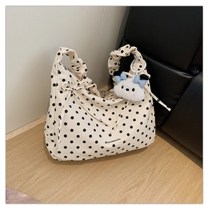 Detail view of cream polka dot tote bag featuring ruched handles and a plush charm