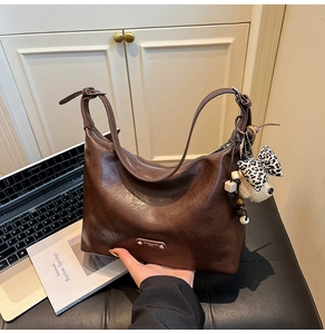 Detail of a dark brown vintage shoulder bag with plush bear charm and metallic logo tag