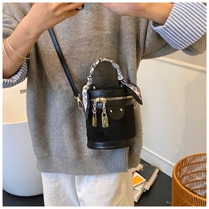 Detail of black cylinder bucket bag featuring gold zippers and scarf-wrapped handle