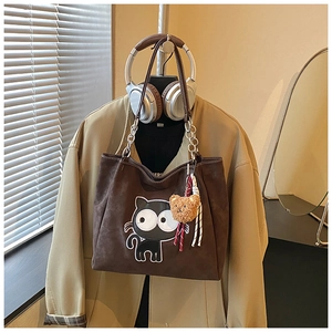 Détail d'un cabas en daim marron avec broderie chat et charm ours sur un manteau