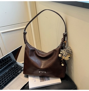 Detail of dark brown oil wax leather shoulder bag with bear pendant and metal logo