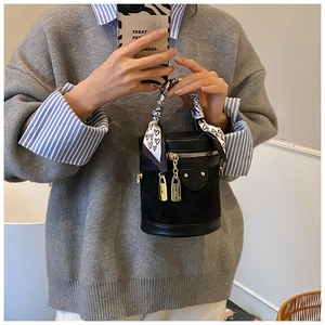 Detail of black cylinder bucket bag with golden studs and decorative heart print scarf