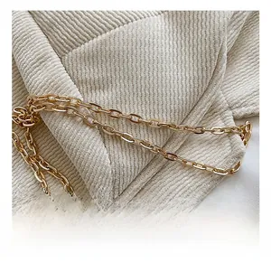 Close-up of golden metal chain strap on light beige corduroy handbag detail