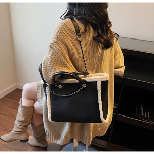 Detail of black suede tote bag with faux fur trim and gold chain handle shown on a shoulder