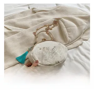 Detail view of bird and flower embroidery on round silk shell bag with blue tassel
