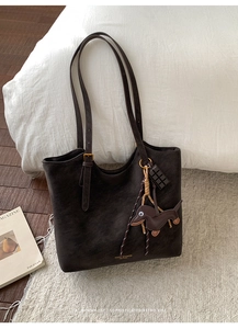 Detail of dark coffee leather tote bag featuring a cute dachshund charm and golden signature