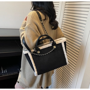 Detail of black suede tote bag with white shearling trim and metal chain accents