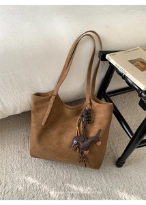 Detail of a brown leather tote bag with a sausage dog charm and chocolate pendant