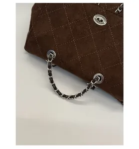 Detail of dark brown suede quilted bag with silver metal chain and twist-lock buckle