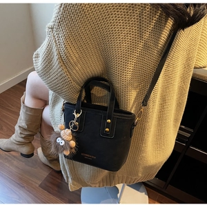 Detail of black matte crossbody bucket bag with brass rivets and a plush monster charm