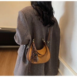 Détail d'un sac hobo en daim marron avec pendentif London et ours sur un manteau gris