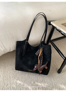 Detail of black tote bag with matte texture, gold hardware, and cute dog bag charm