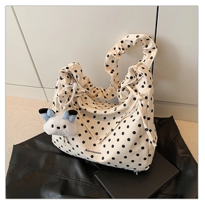 Close-up of beige polka dot canvas bag with pleated handle and plush cat charm