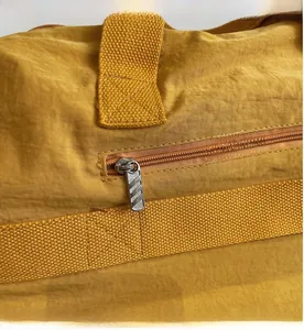 Detail of smooth metal zipper and durable fabric handle on yellow travel duffel bag