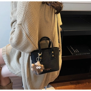 Detail of black mini crossbody bucket bag with gold rivets and brown plush monster charm