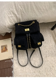 Detail of black quilted suede backpack with golden turn-lock fasteners on white fur rug