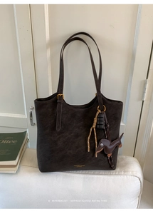 Detail of dark brown leather tote bag with logo and dachshund charm on a white background