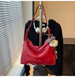 Detail of red crescent hobo bag with plush bear charm and metallic brand logo plaque