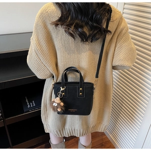 Detail of a black canvas mini tote with gold lettering and a brown plush charm accessory