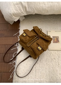 Detail view of brown suede backpack with quilted pockets and gold chain on plush rug