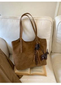 Detail view of a large vintage brown tote bag on a white sofa with a cute animal charm