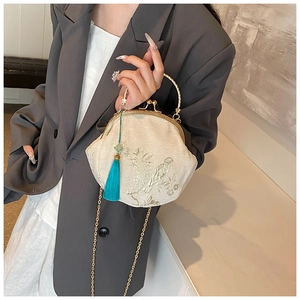 Detail of embroidered silk shell bag featuring golden bird patterns and a blue tassel