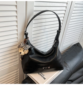 Detail of black faux leather hobo bag with silver hardware and leopard bow bear charm