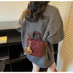 Detail view of burgundy matte leather bucket bag with gold hardware and plush charm