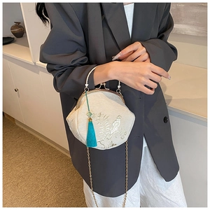 Detail of cream satin shell bag with flower embroidery and blue tassel charm