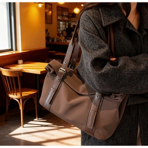 Détail du sac cabas marron montrant les plis latéraux et la boucle de sangle ajustable