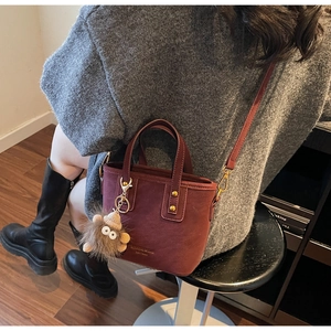 Detail of burgundy frosted bucket bag with gold hardware and plush hedgehog charm