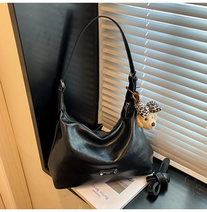 Detail of black leather hobo bag with metal logo and cute dog plush charm on strap
