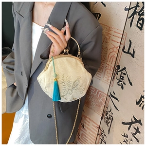 Detail of embroidered shell bag with bird patterns, gold metal clasp and green tassel