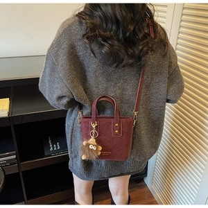 Detail of burgundy bucket bag with golden hardware and cute brown plush monster charm