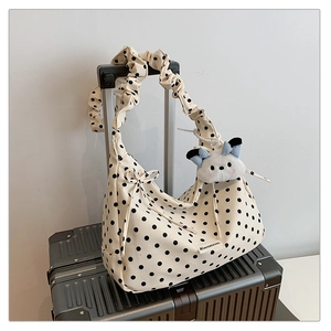 Polka dot canvas dumpling bag with ruched strap and plush charm on a silver suitcase