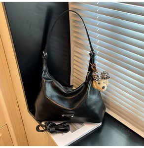 Close-up of black PU leather Hobo bag with plush dog charm and metal logo detail