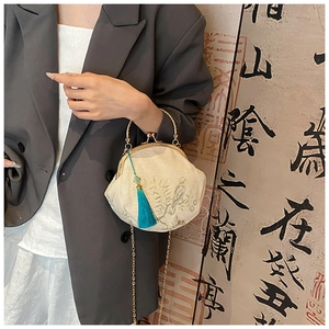 Detail of embroidered floral shell bag with metal kiss lock and blue tassel accent