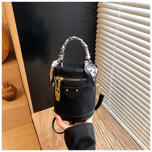 Detail of black cylindrical bucket bag with gold hardware and silk scarf handle